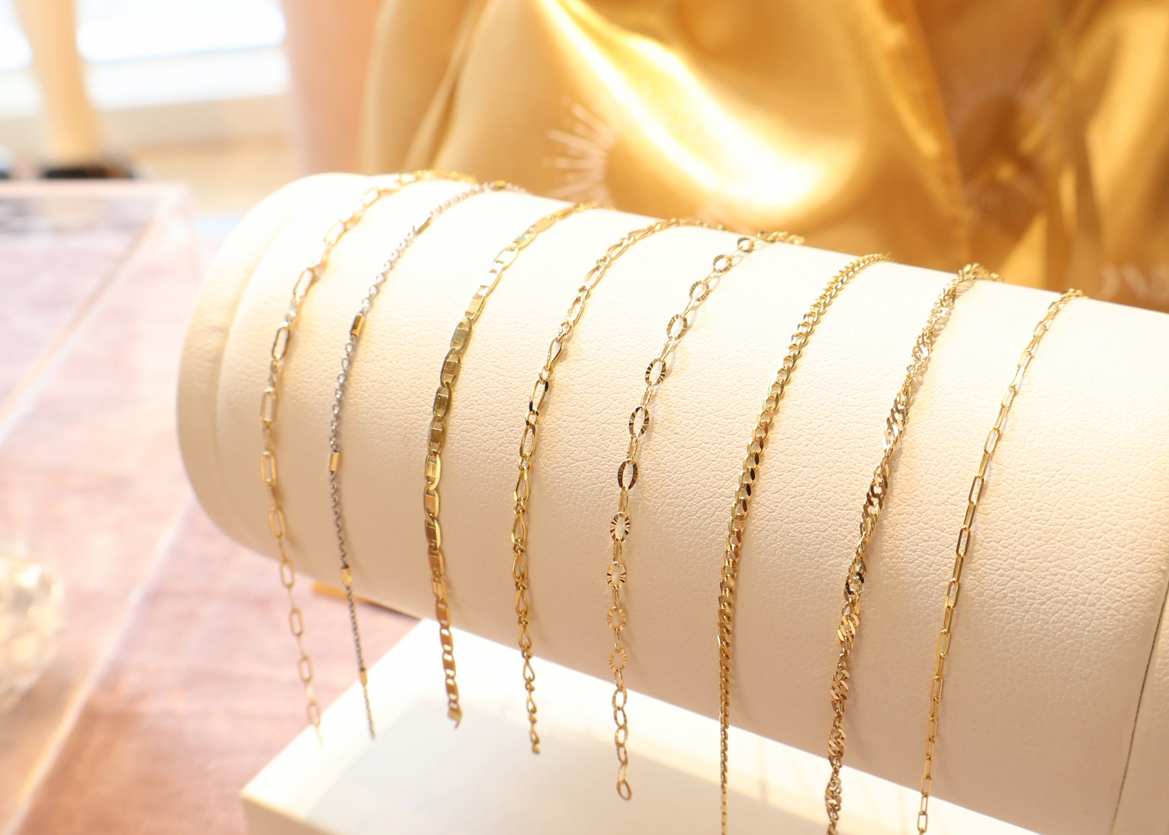 14k Gold bracelets on a white stand with a gold satin Golden Bond Jewelry bag in the background