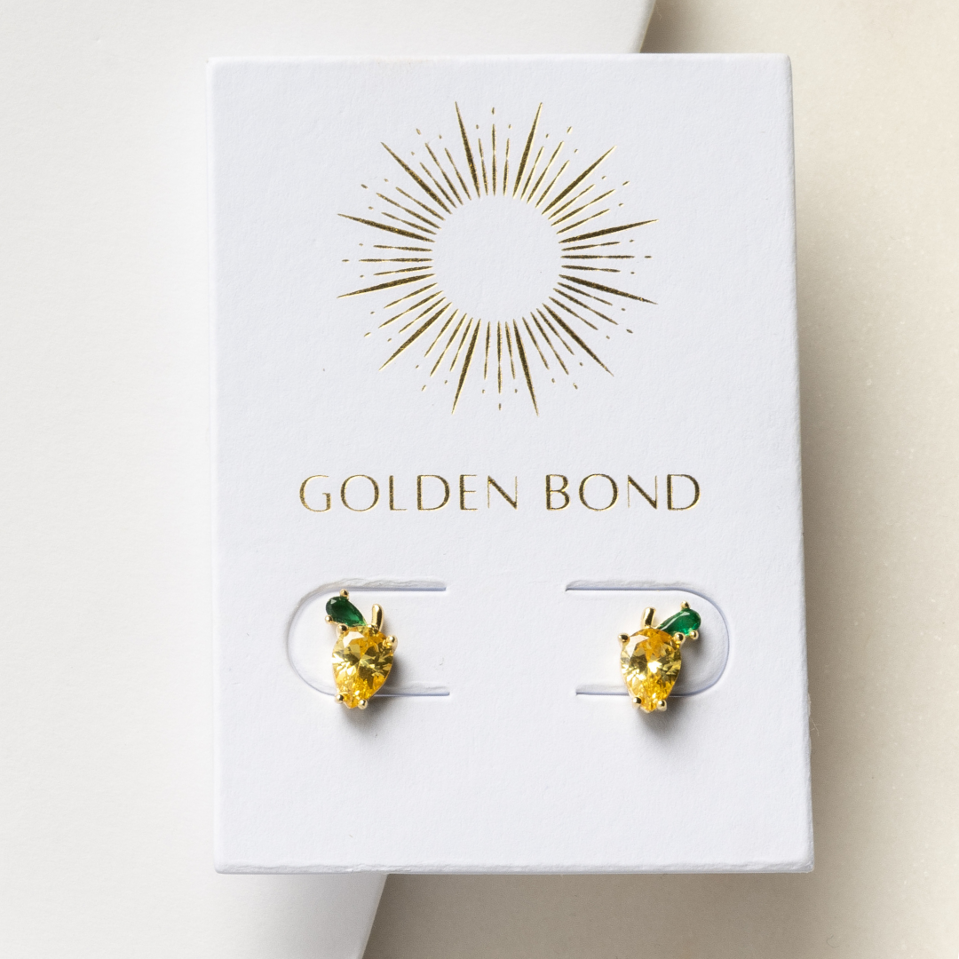 A pair of gold stud earrings with lemon-yellow stones and green leaf accents, presented on a white card with 'GOLDEN BOND' written at the top.