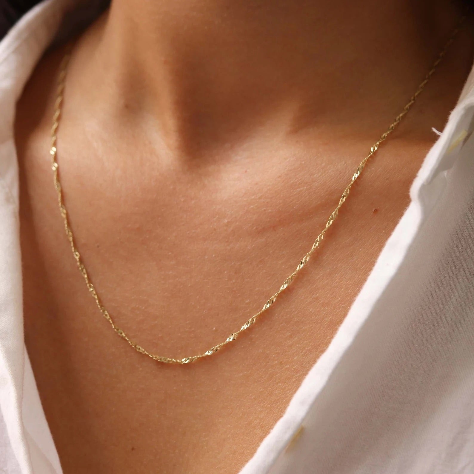 Gold necklace on a person wearing a white shirt