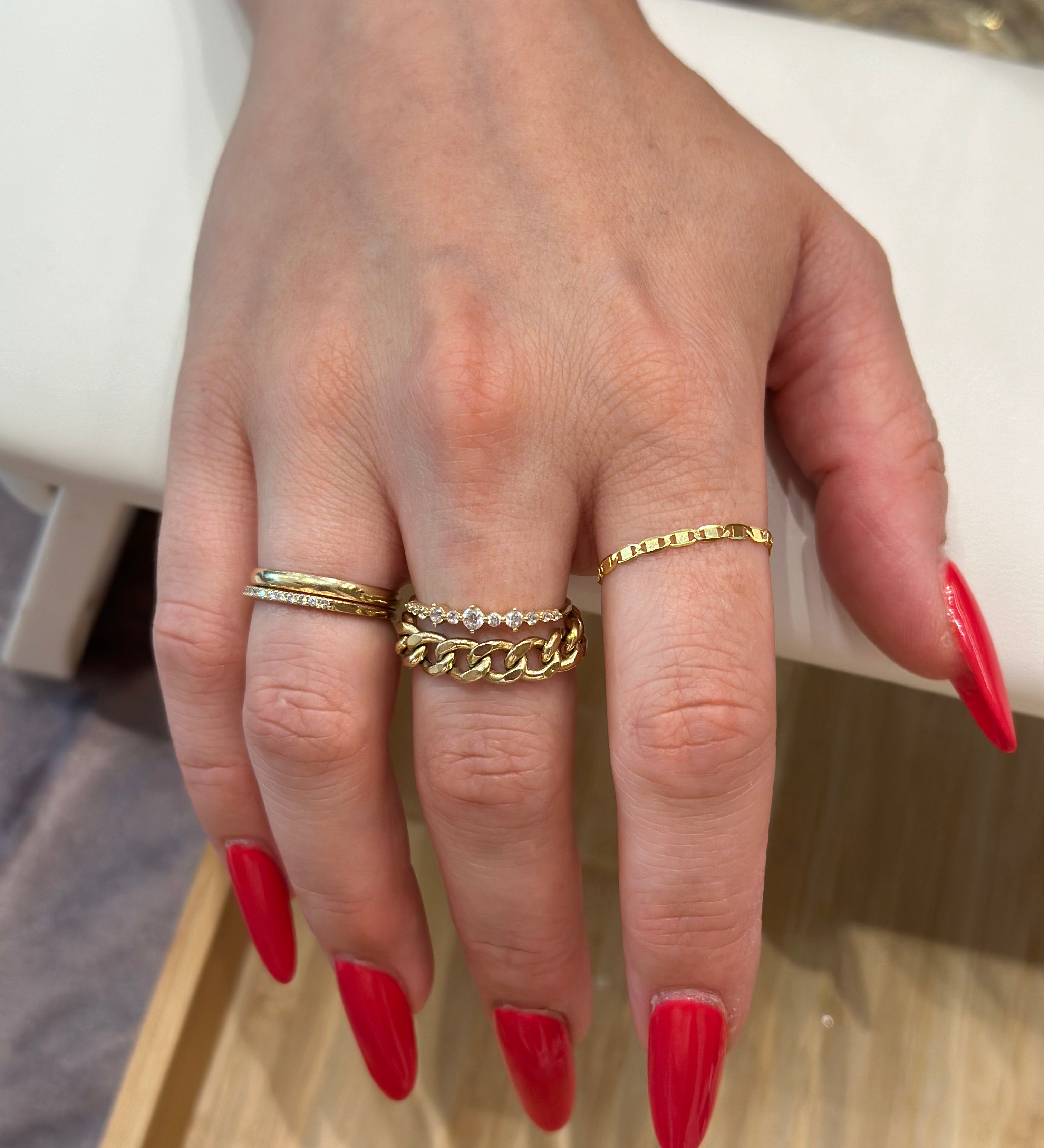 A person's hand showcasing a gold infinity chain ring custom made by Golden Bond Jewelry. The woman has red nail polish on.