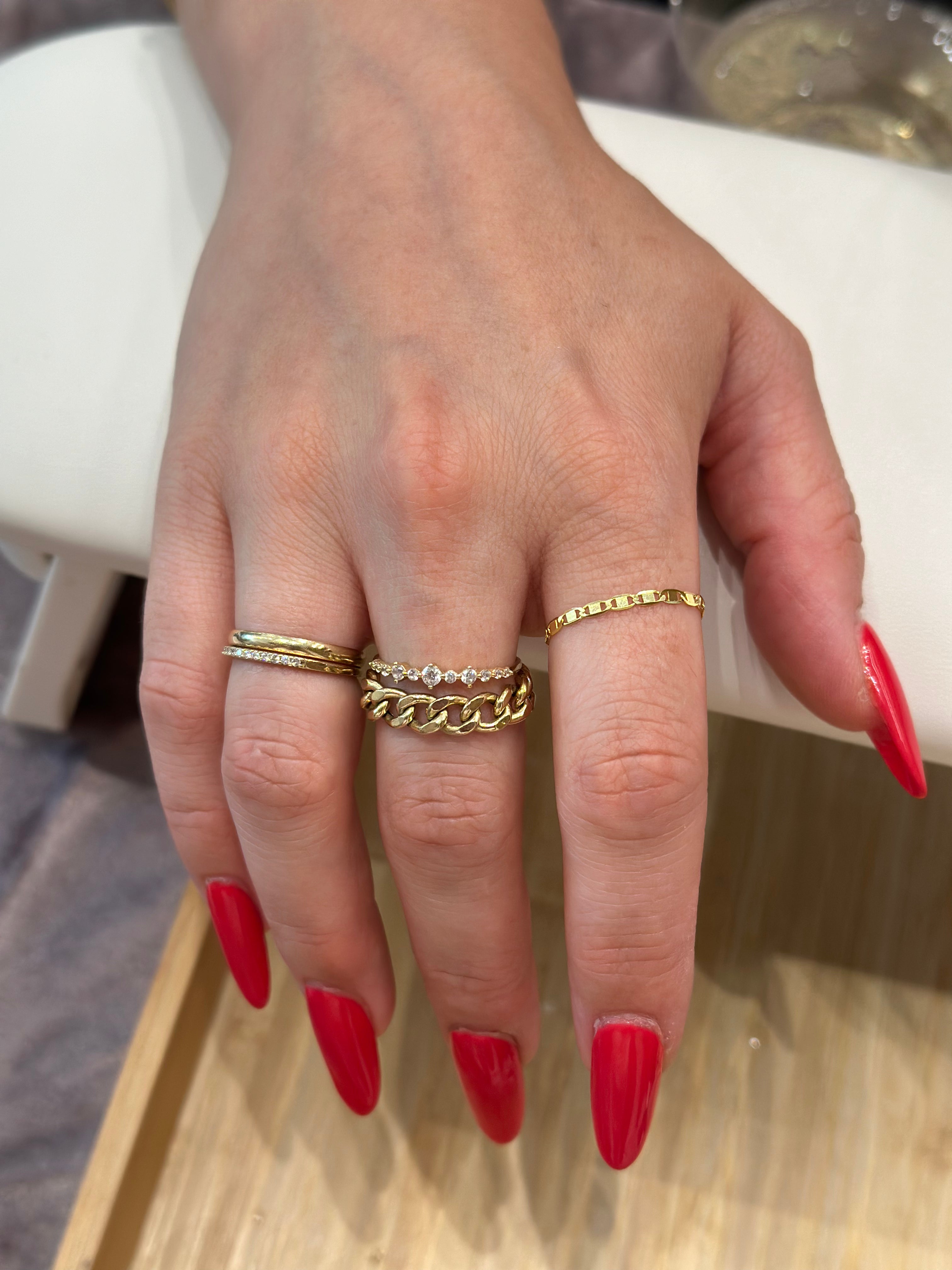 A person's hand showcasing a gold infinity chain ring custom made by Golden Bond Jewelry. The woman has red nail polish on.