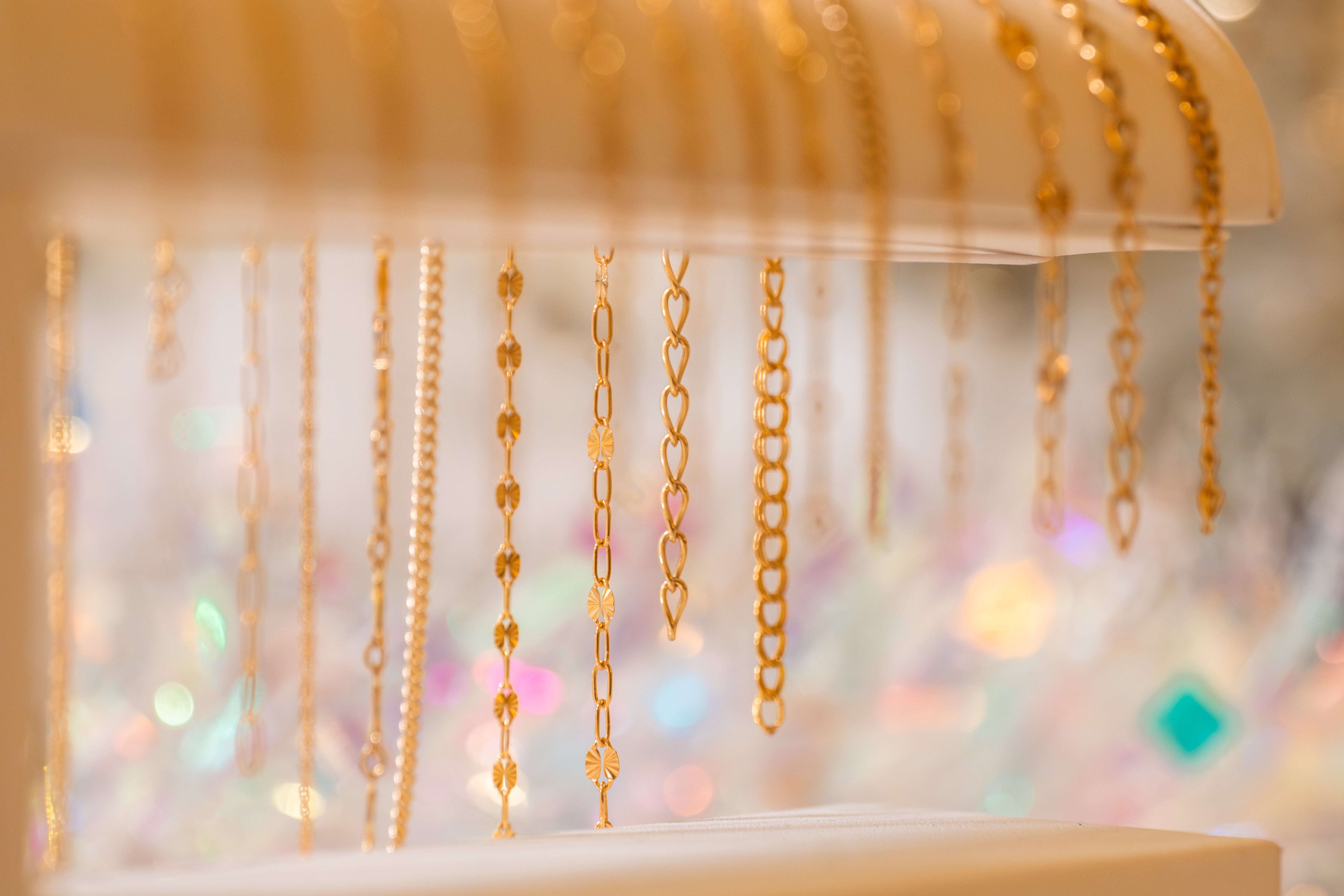 Gold chains hanging on a display stand with a blurred colorful background