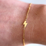 Gold bracelet with a lightning bolt charm on a wrist.