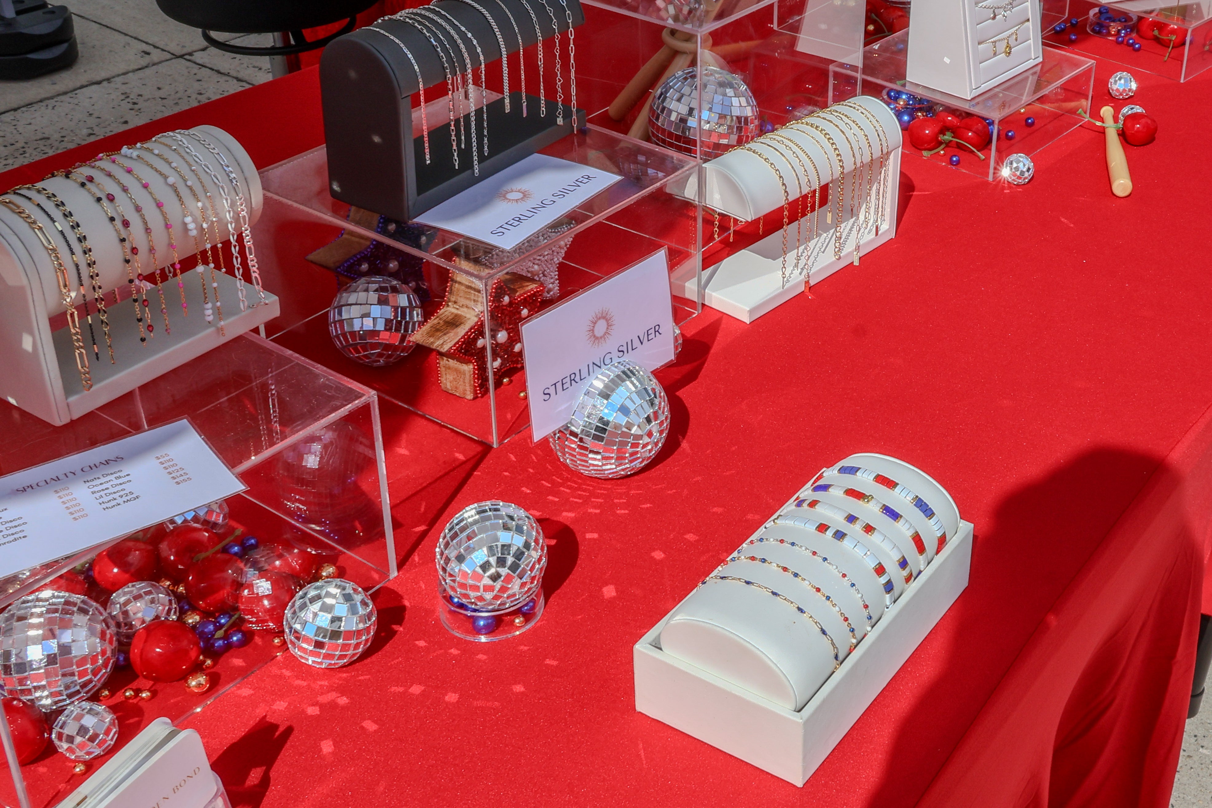 Display of jewelry including bracelets and disco balls on a red table at Nat's Park in Washington, DC