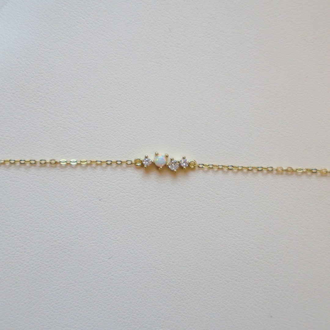 Gold bracelet with one opal and three small diamonds on a white leather surface