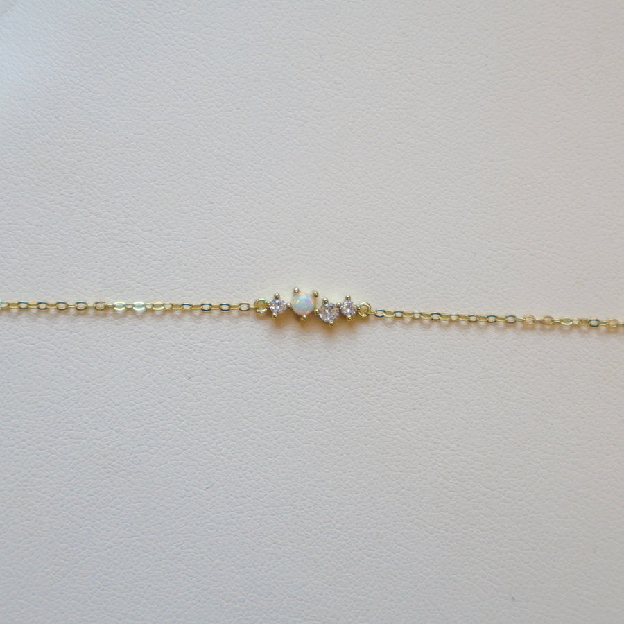 Gold bracelet with one opal and three small diamonds on a white leather surface