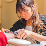Woman getting a permanent jewelry in a festive setting with Christmas decorations.