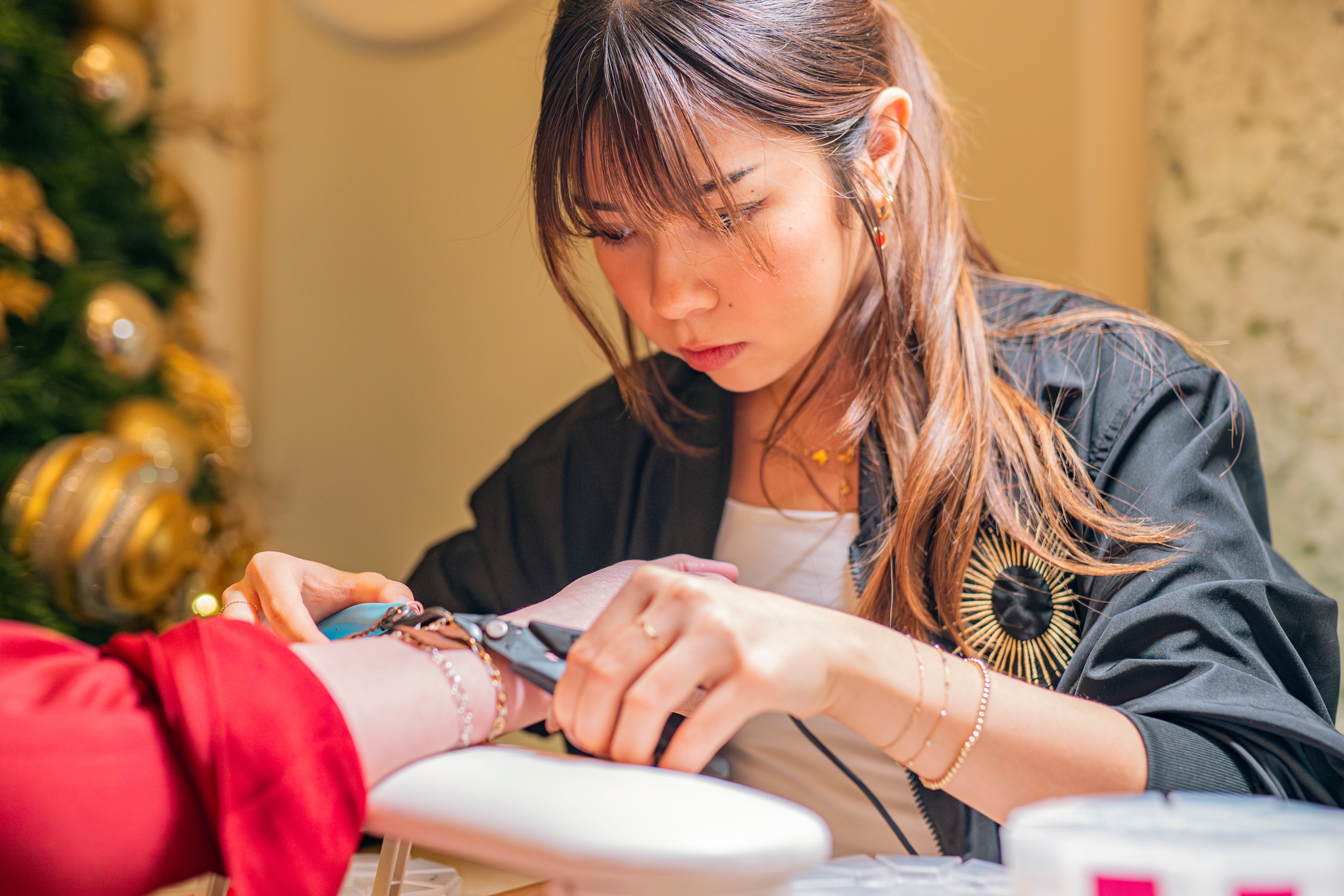 Woman getting a permanent jewelry in a festive setting with Christmas decorations.